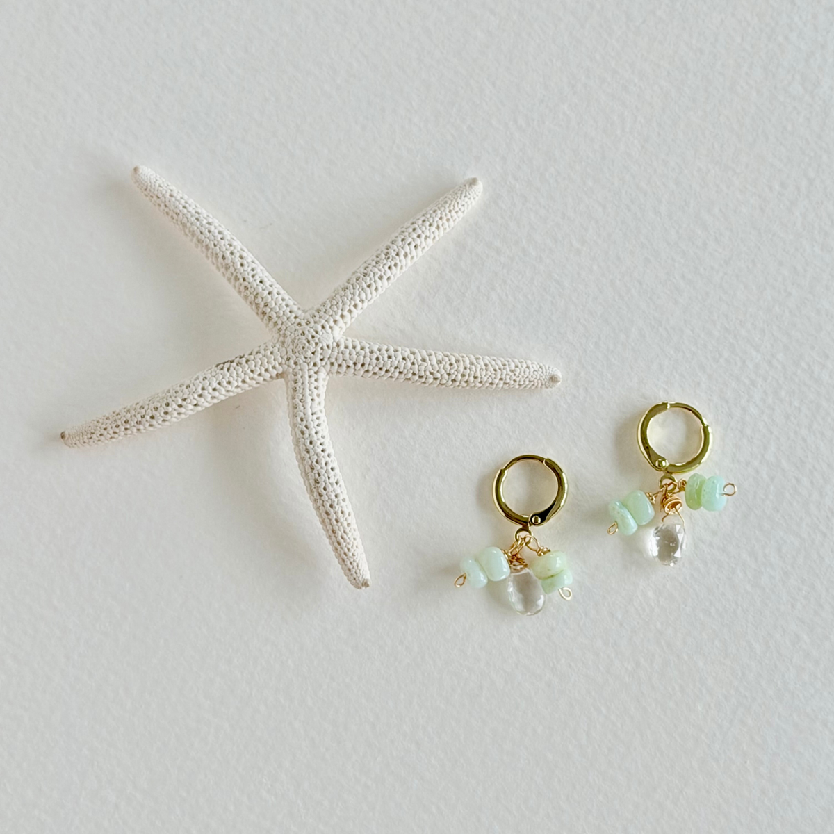 Pair of gold earrings with green beads on a white surface with a starfish.