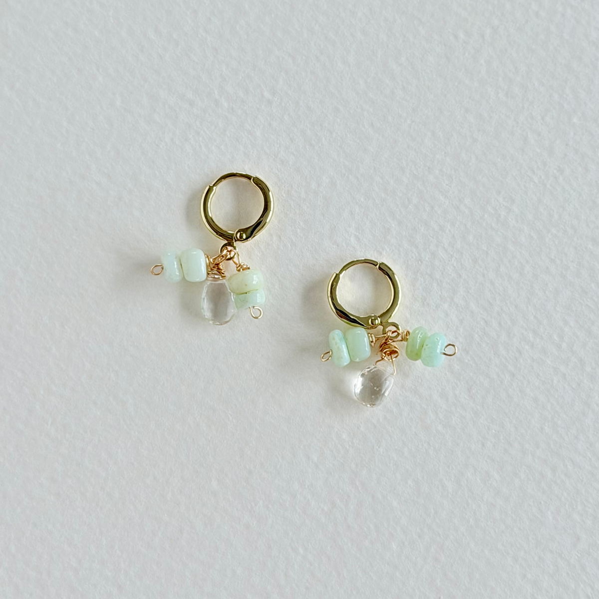 Gold hoop earrings with clear and green beads on a light gray background