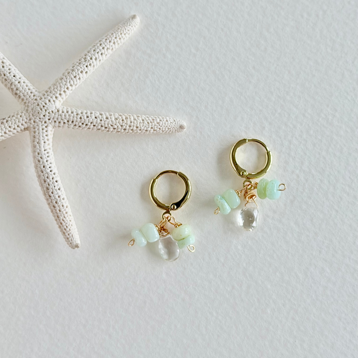 Gold hoop earrings with green beads on a white background with a starfish.