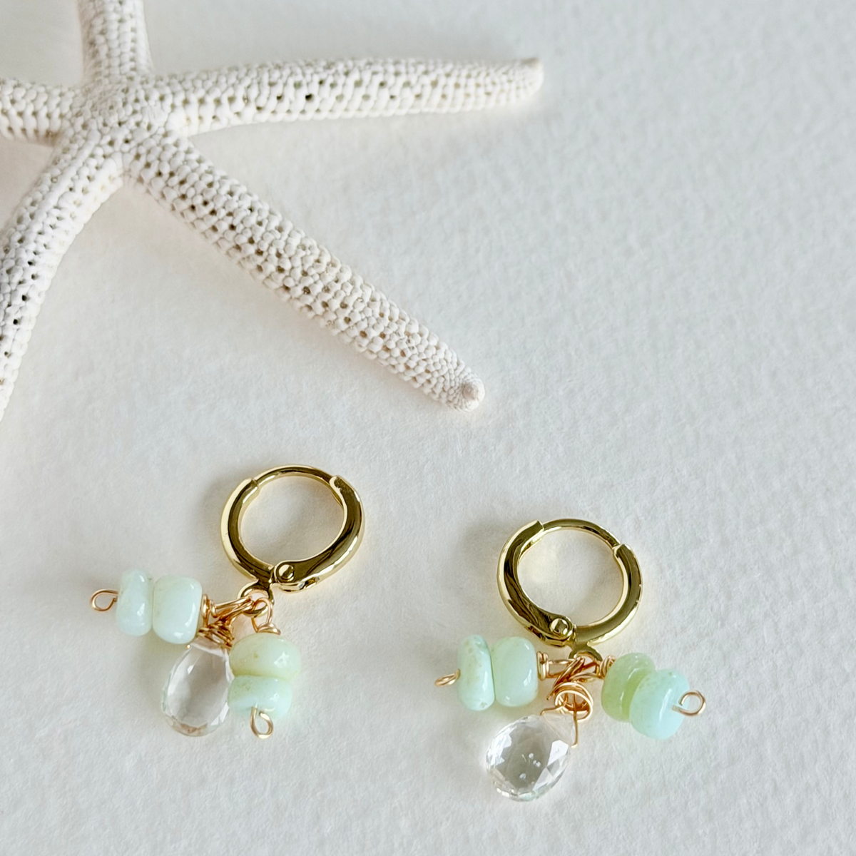 Gold hoop earrings with green and clear beads on a white background with starfish.