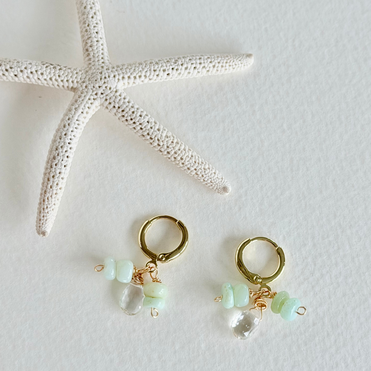 Gold hoop earrings with green beads on a white surface with a starfish.