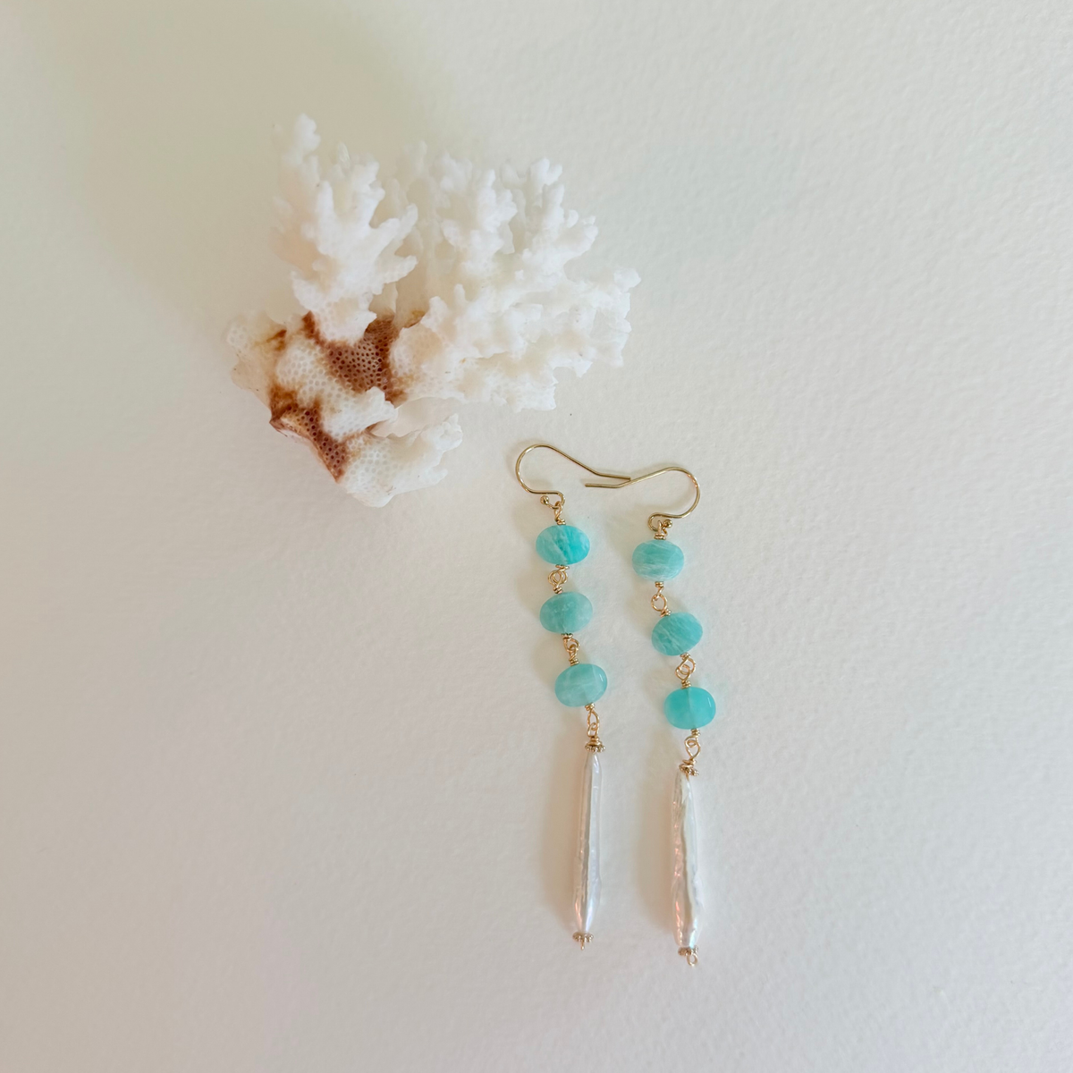 Turquoise beaded earrings with gold accents on a light background with coral.