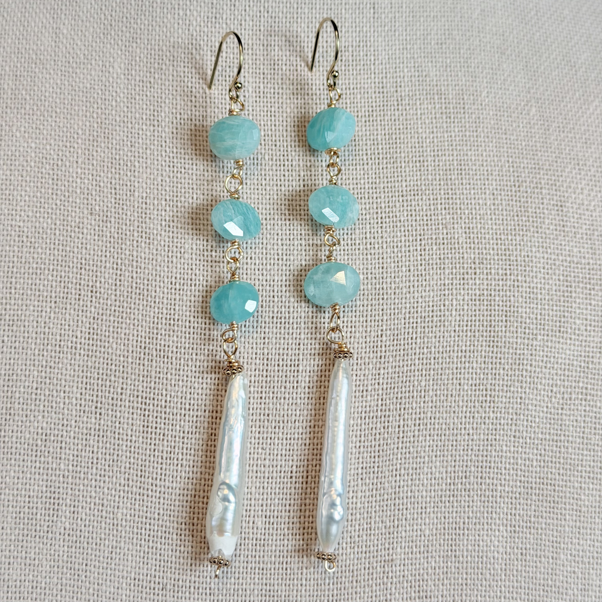 Pair of earrings with turquoise beads and pearl-like drops on a light gray background