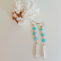 Pair of earrings with turquoise beads and a white shell pendant on a light background.