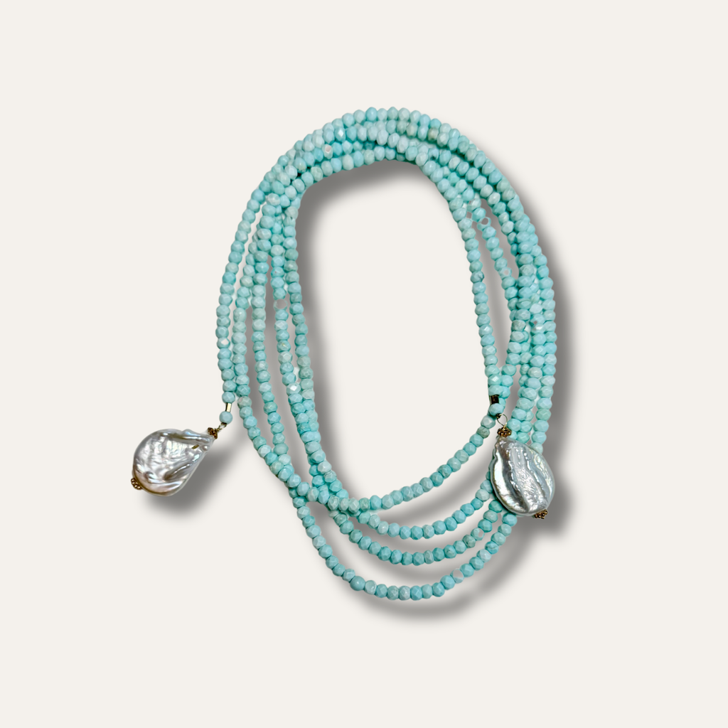 A multi-strand beaded necklace featuring light turquoise blue beads and two textured, clear teardrop-shaped crystal pendants, displayed on a light beige background.