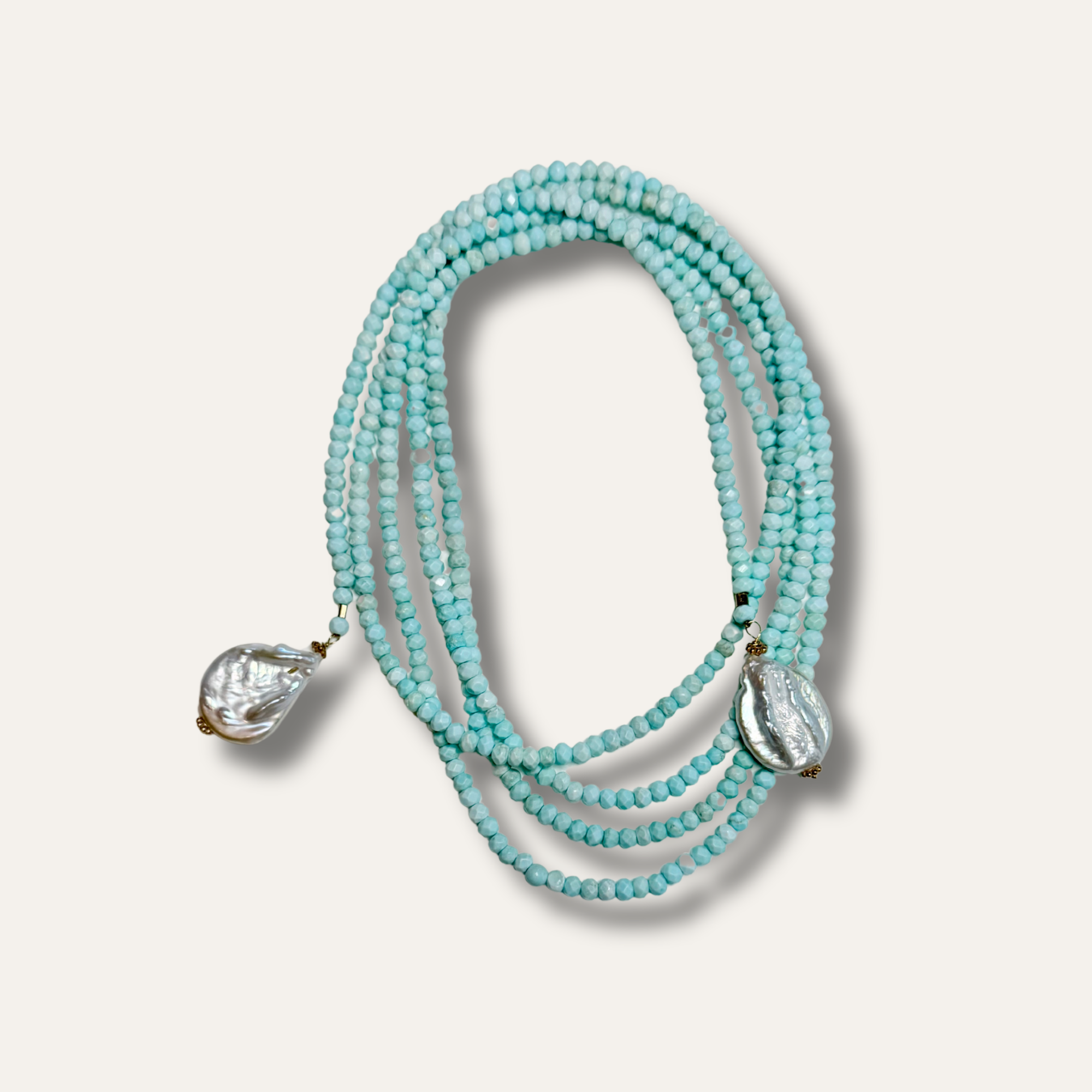 A multi-strand beaded necklace featuring light turquoise blue beads and two textured, clear teardrop-shaped crystal pendants, displayed on a light beige background.