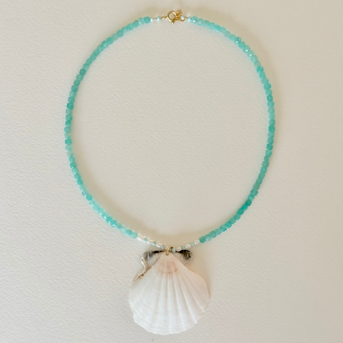 Necklace with turquoise beads and a shell pendant on a light background