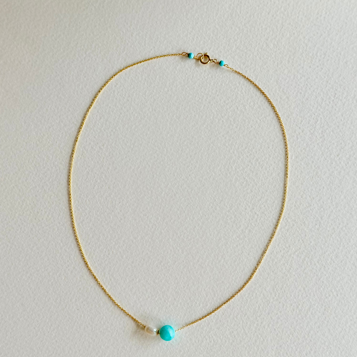Gold necklace with turquoise beads on a light gray background