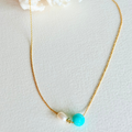 Necklace with gold chain, turquoise bead, and pearl on a light background