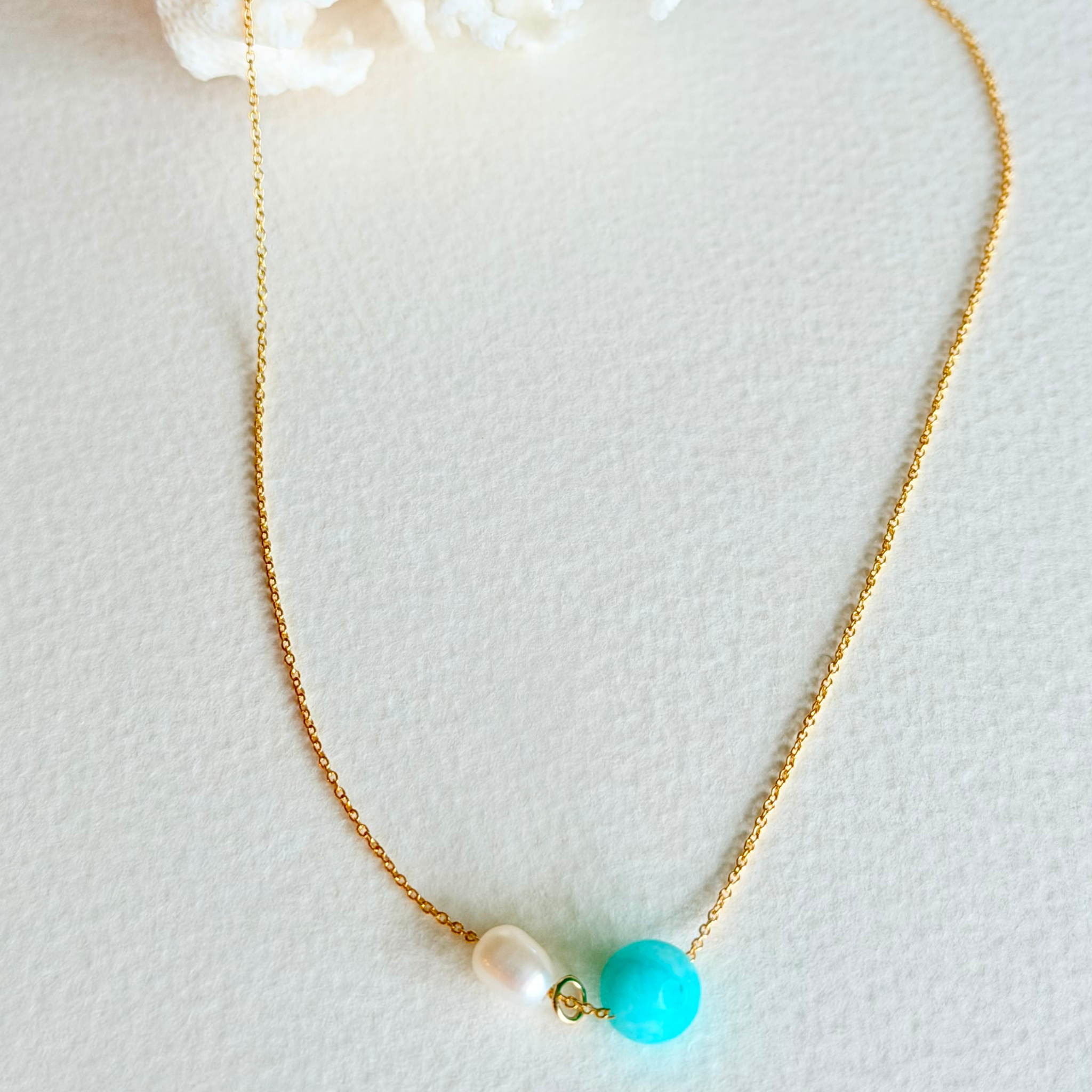 Necklace with gold chain, turquoise bead, and pearl on a light background