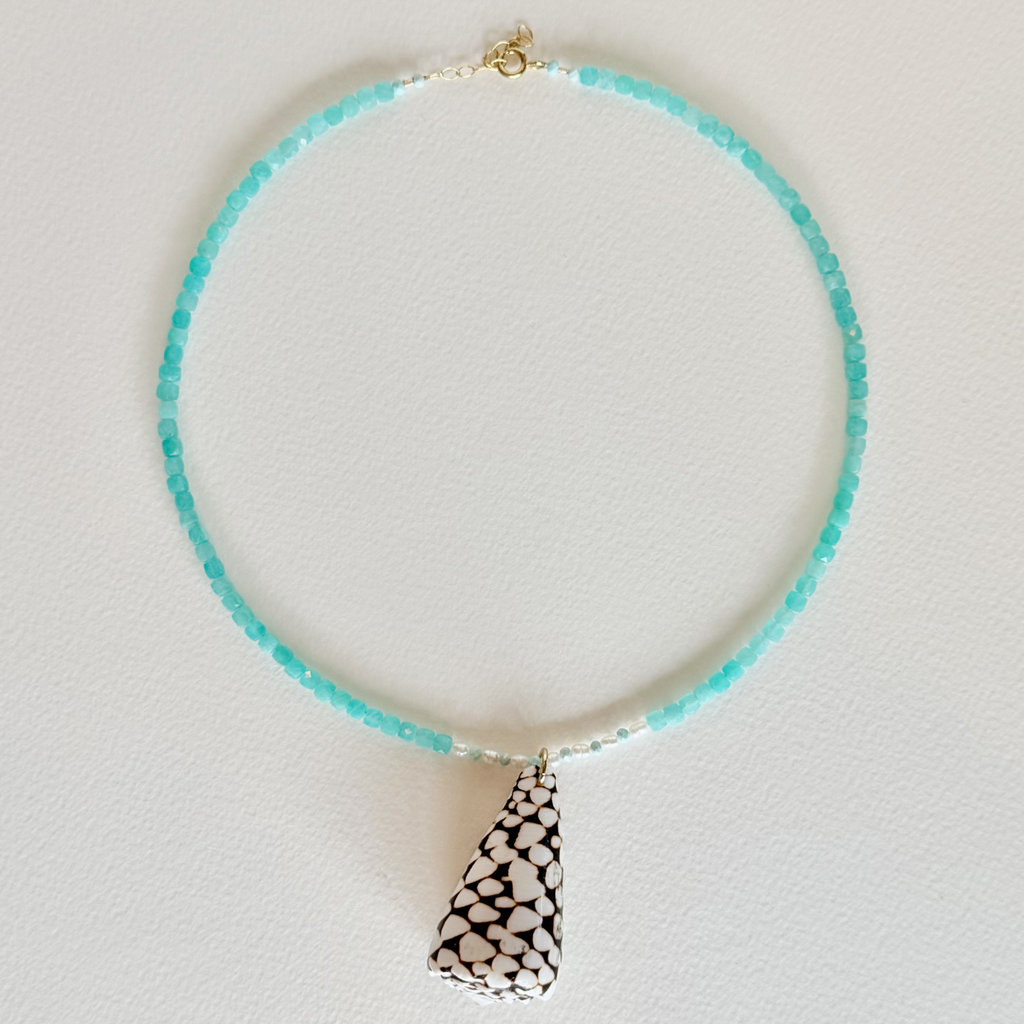 Necklace with turquoise beads and a patterned pendant on a light gray background