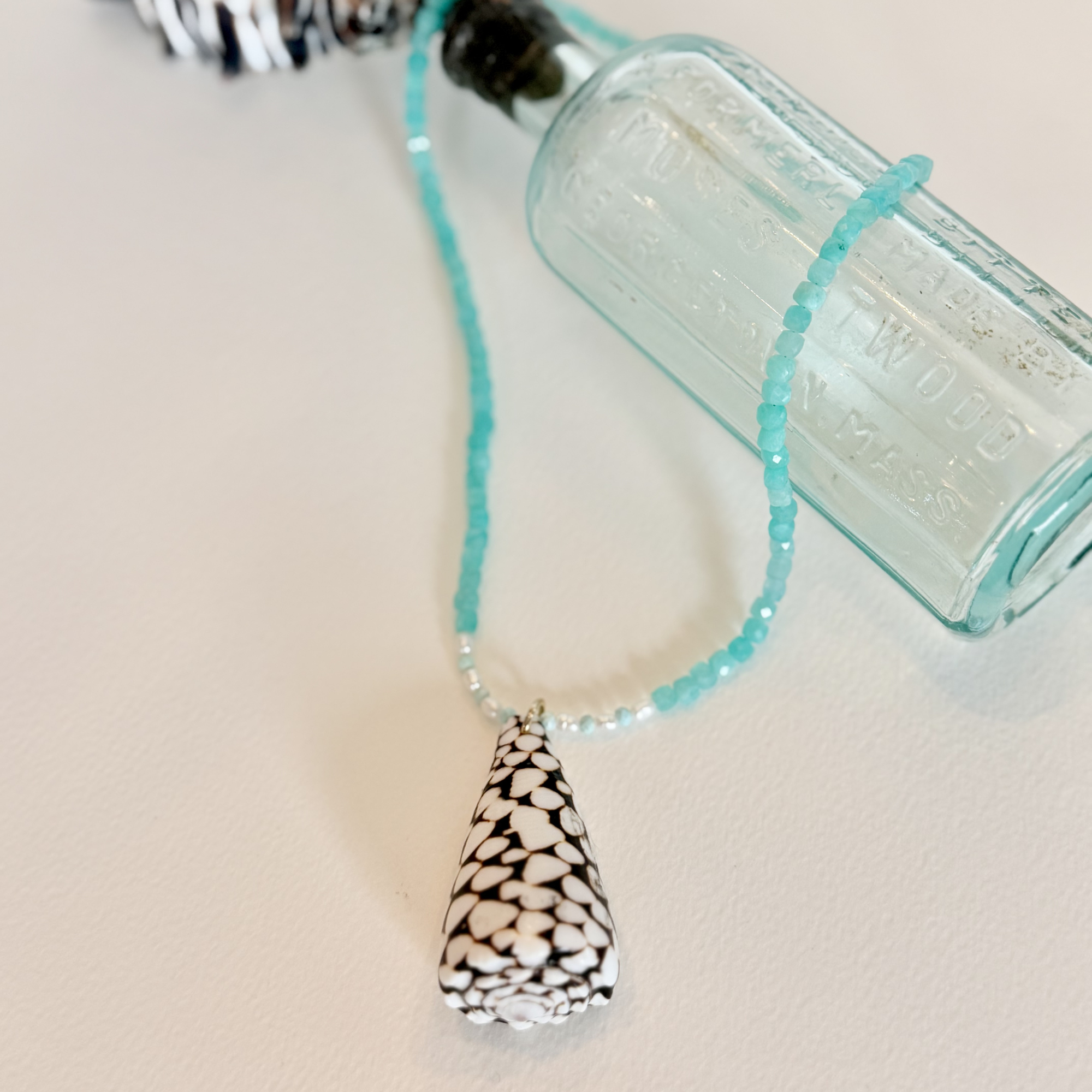 Necklace with a teardrop-shaped pendant next to a vintage bottle on a light background
