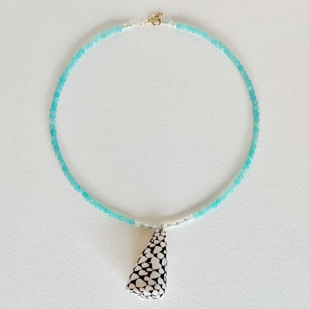 Necklace with turquoise beads and a black and white patterned pendant on a light gray background