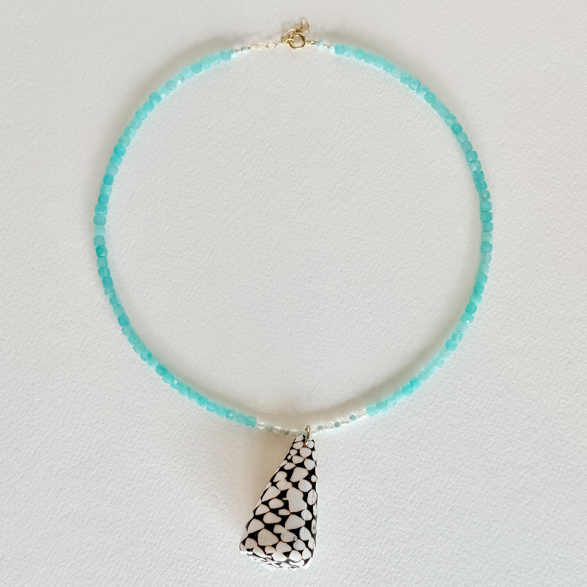 Necklace with turquoise beads and a black and white patterned pendant on a light gray background