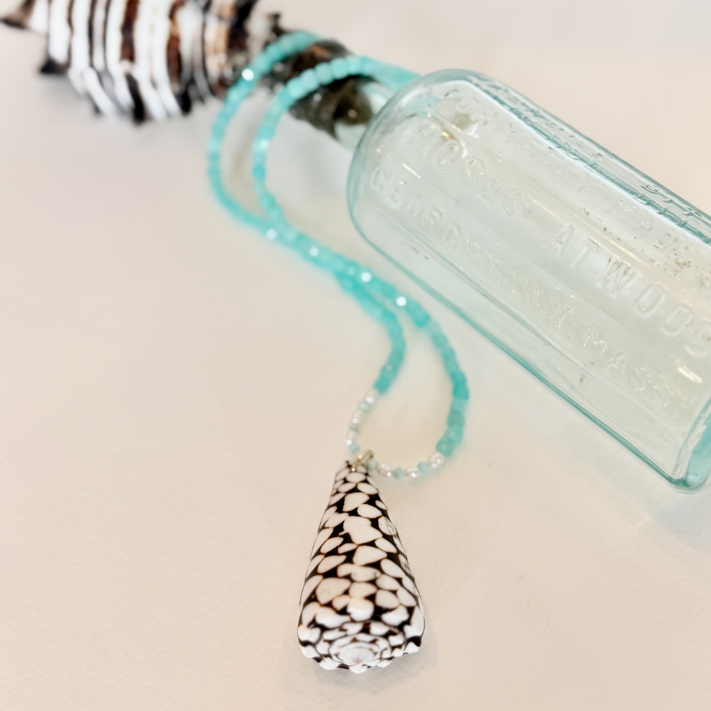Necklace with a shell pendant and turquoise beads next to a clear bottle on a light background