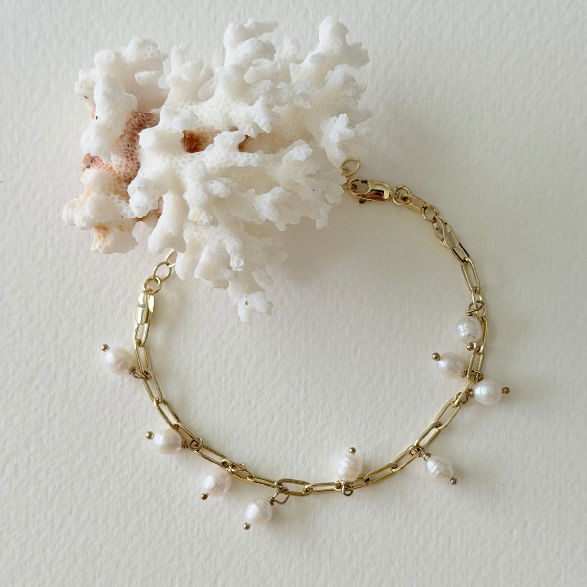 Gold bracelet with pearls on a white background with coral