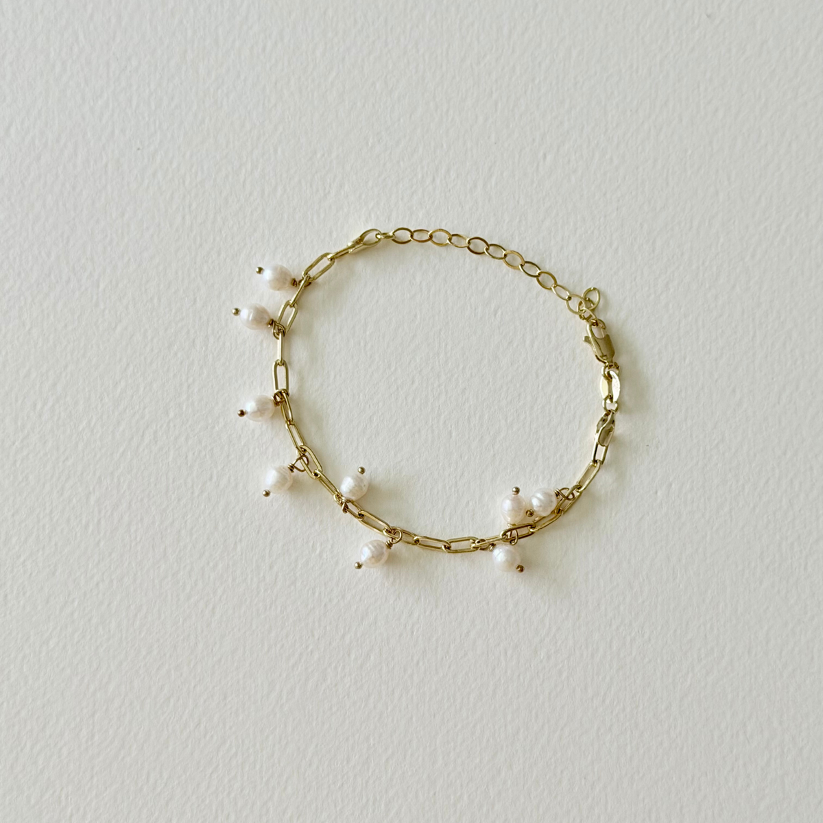 Gold bracelet with small pearls on a light gray background