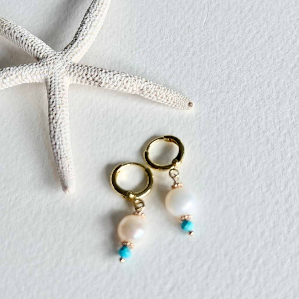Gold hoop earrings with pearls and turquoise beads on a light gray background with a starfish.