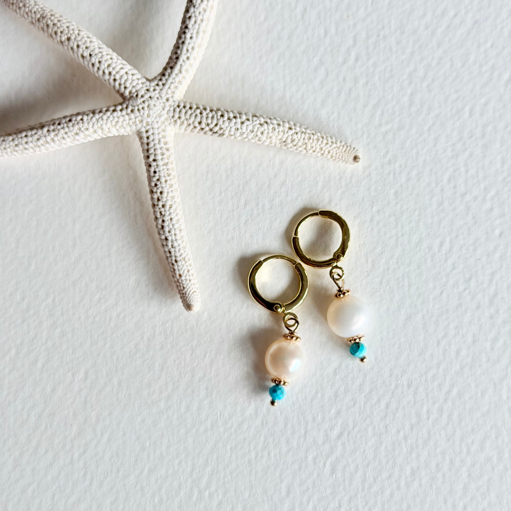Gold earrings with pearls and turquoise beads on a white background with a starfish.