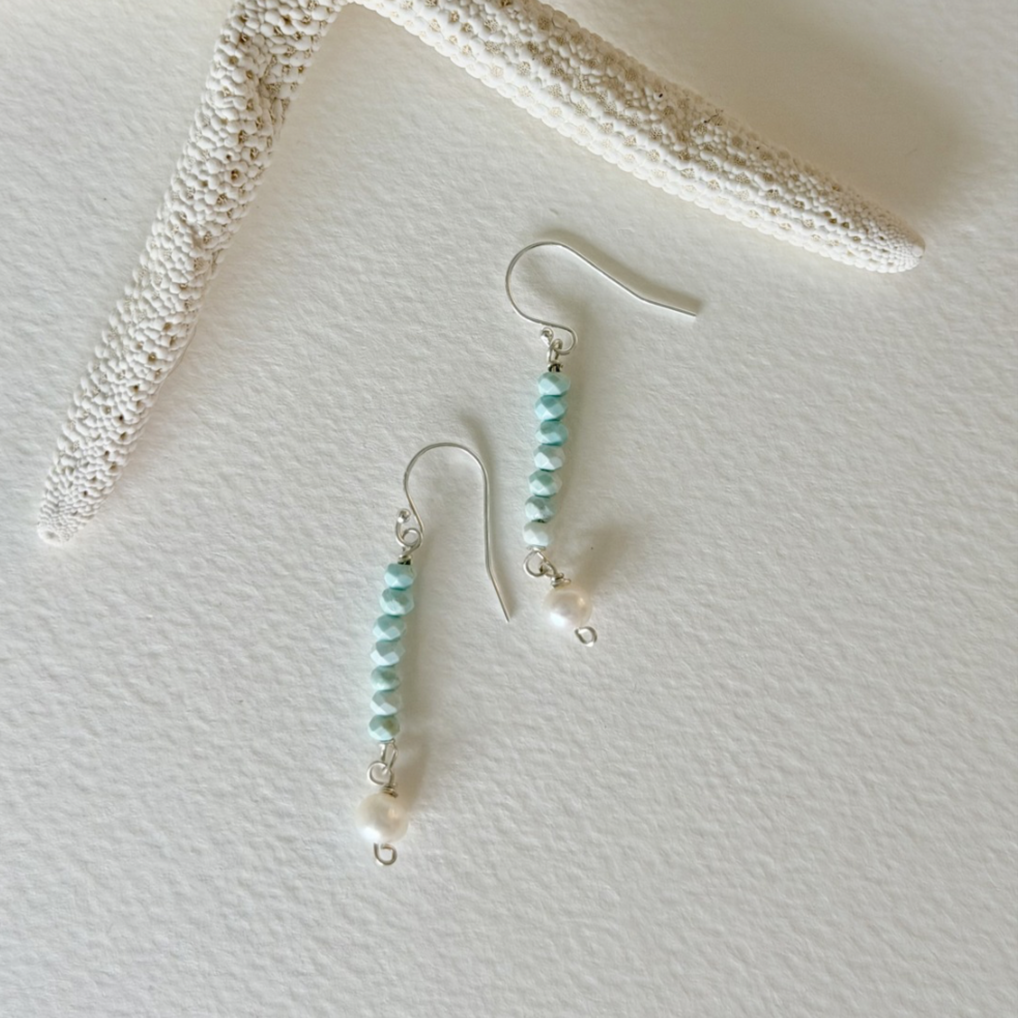 Pair of earrings with turquoise beads on a textured white surface
