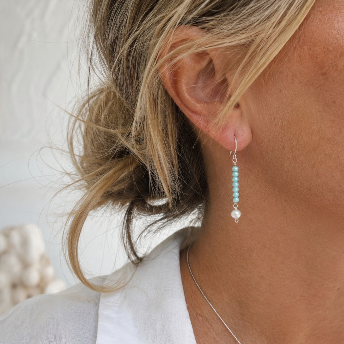 Close-up of a person wearing turquoise beaded earrings with a blurred background