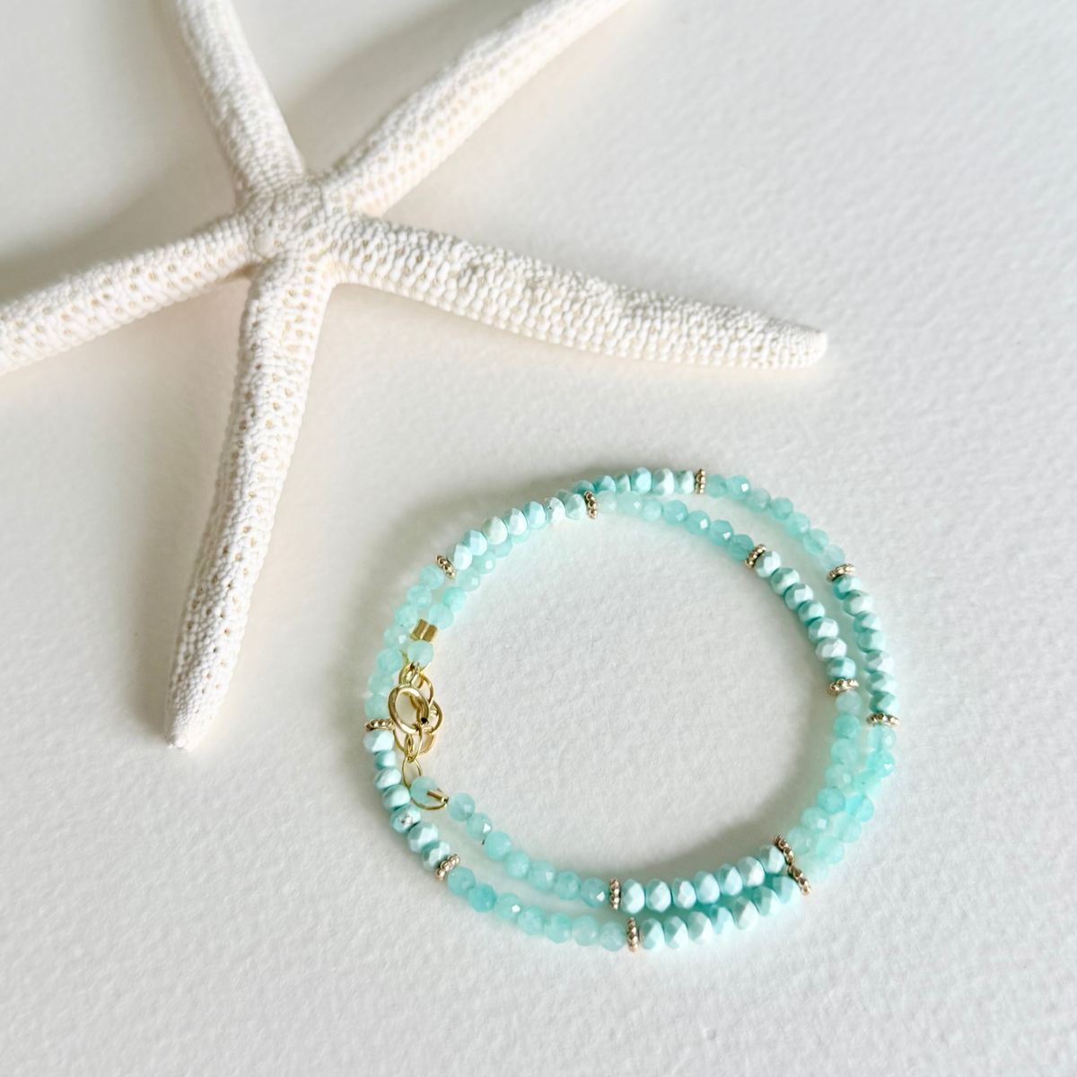 Turquoise beaded bracelet with gold accents on a white surface with a starfish.