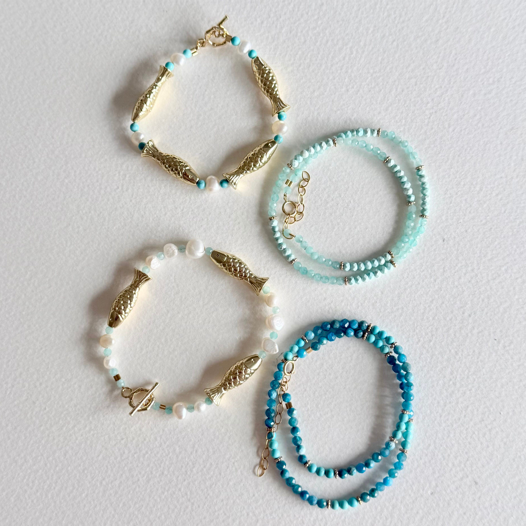 Set of three beaded bracelets with gold fish charms on a light gray background