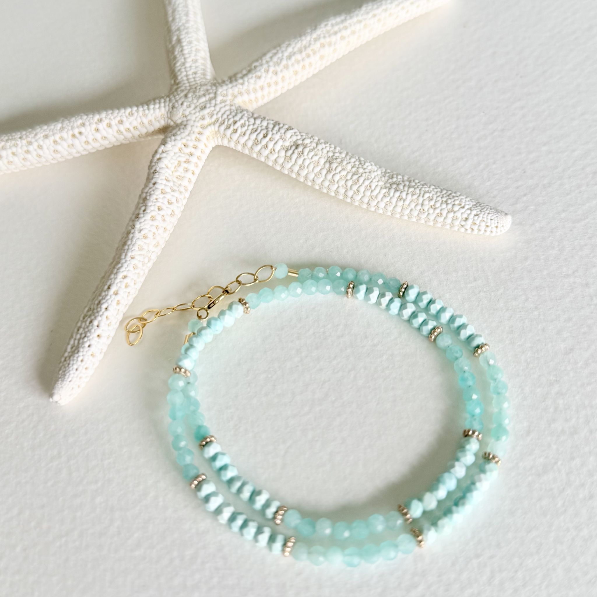 Turquoise beaded bracelet with gold accents on a white surface with a starfish.