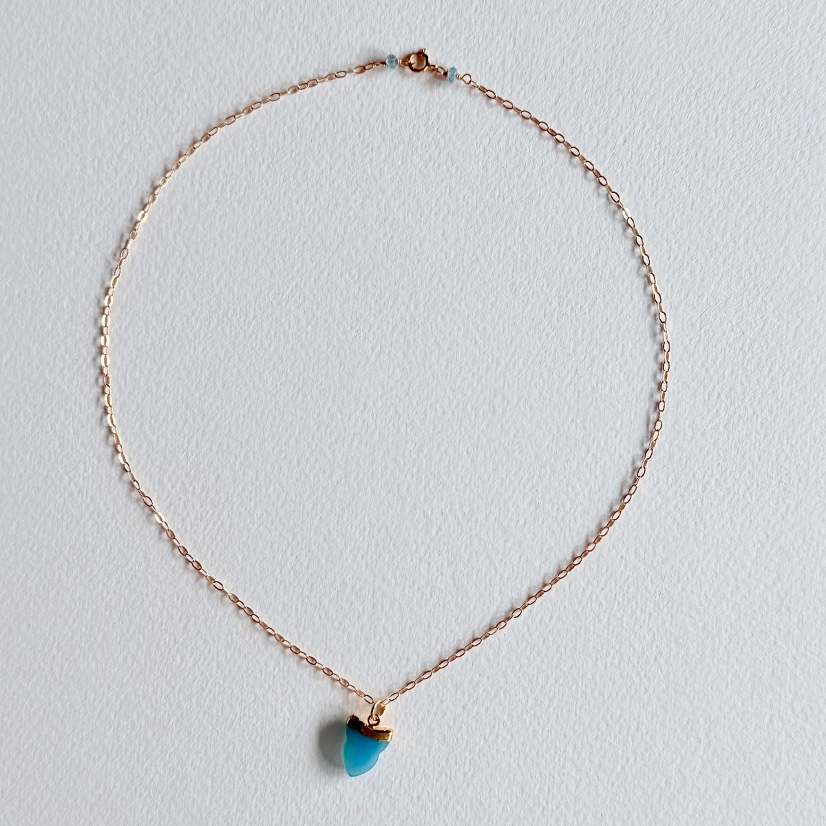 gold necklace with a turquoise pendant on a light gray background