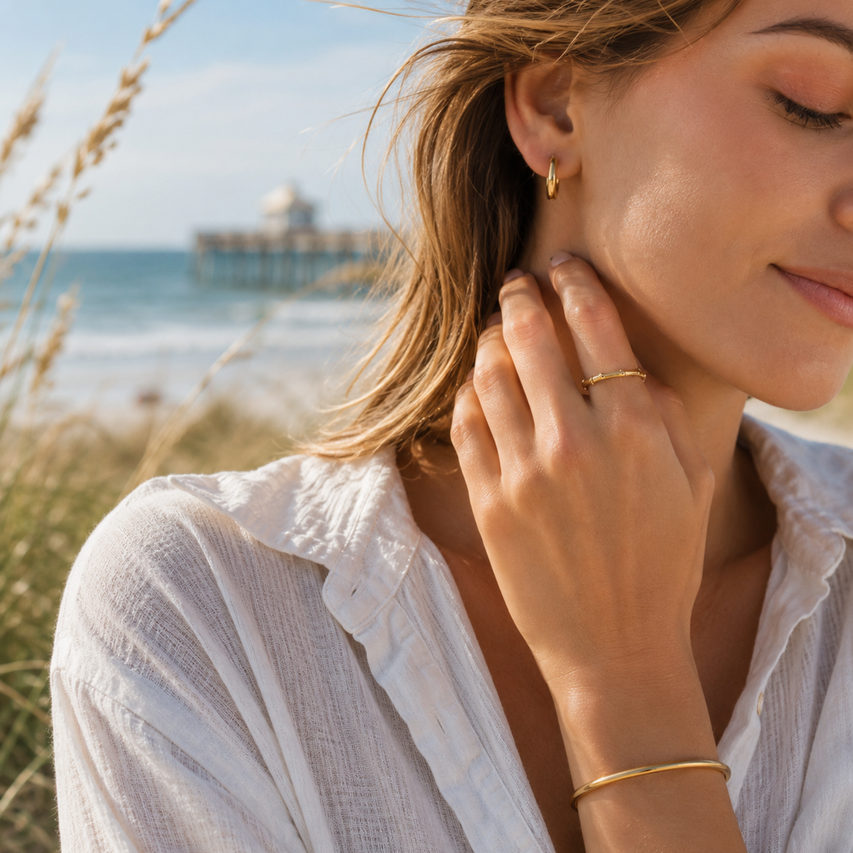 Woman adjusting earring with beach and ocean in the background