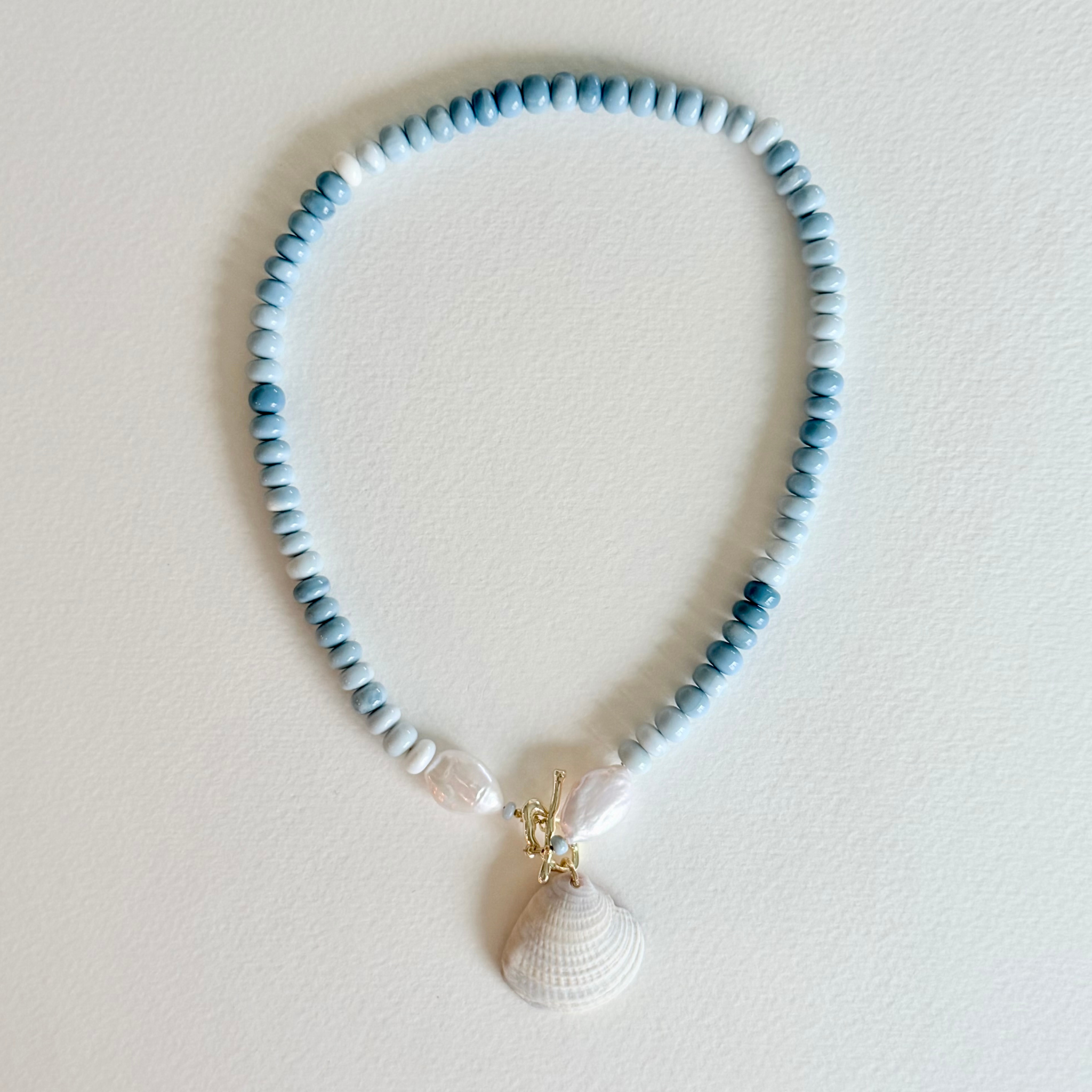Necklace with blue beads and a shell pendant on a light background