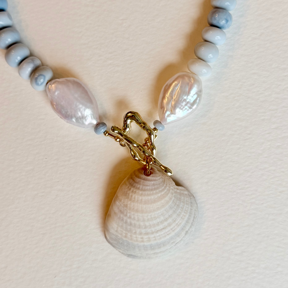 Necklace with shell pendant and gold clasp on a light pink background