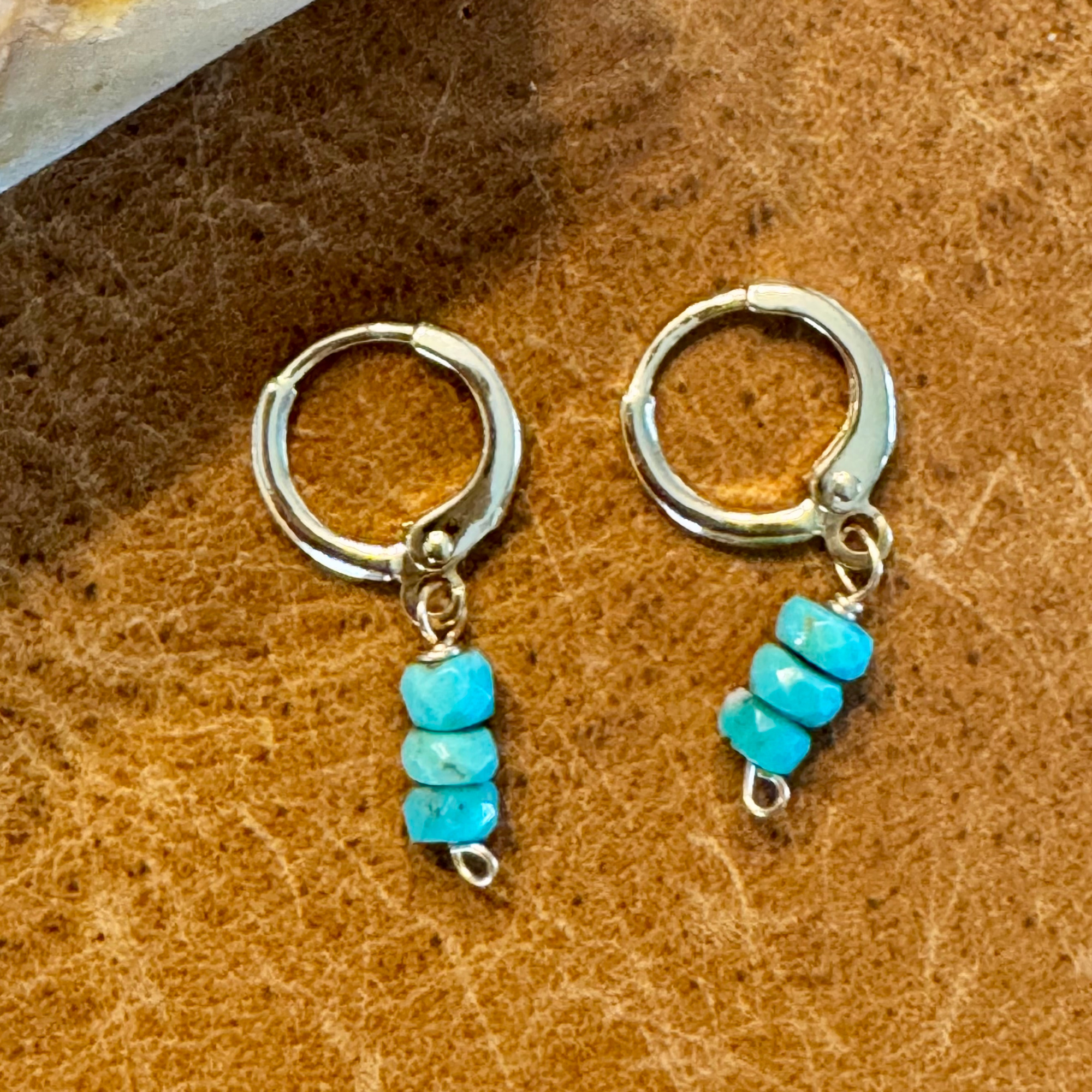 Close up view of gold-filled huggie earrings made with three wide round turquoise blue green stones stacked vertically, displayed against a warm orange yellow brown background.
