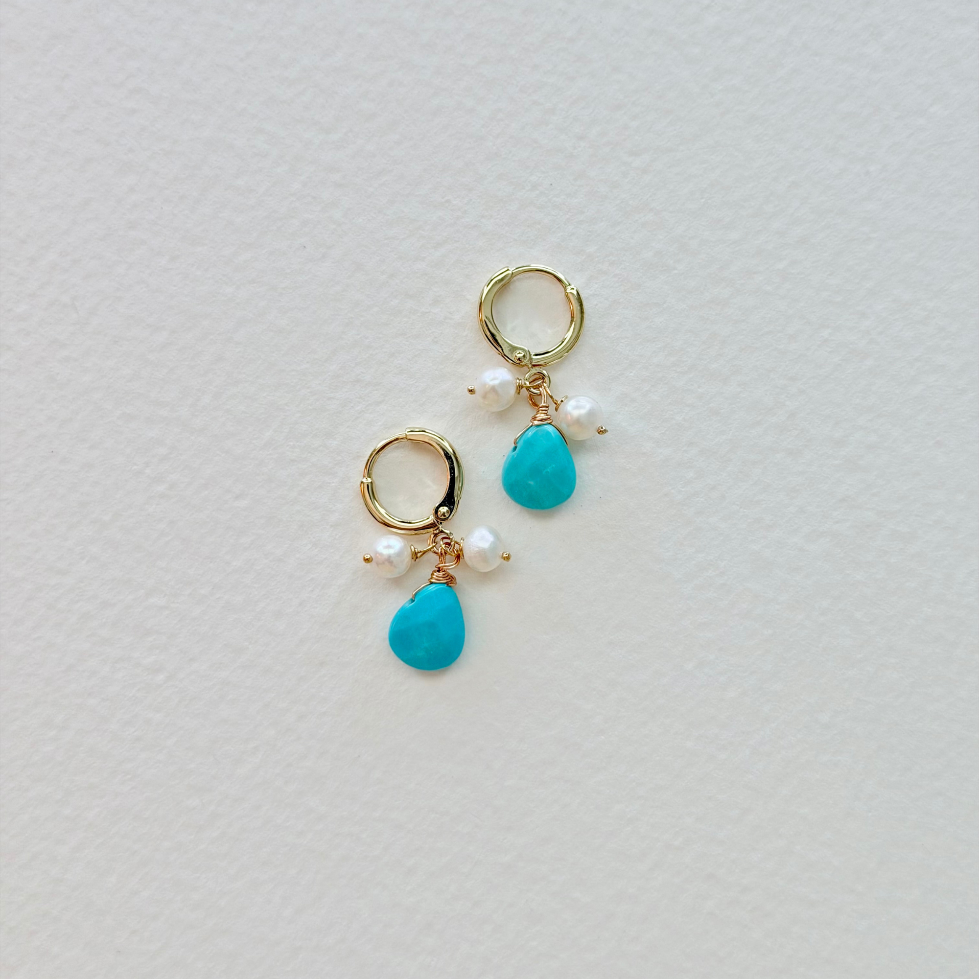Pair of earrings with turquoise drops and gold hooks on a light gray background