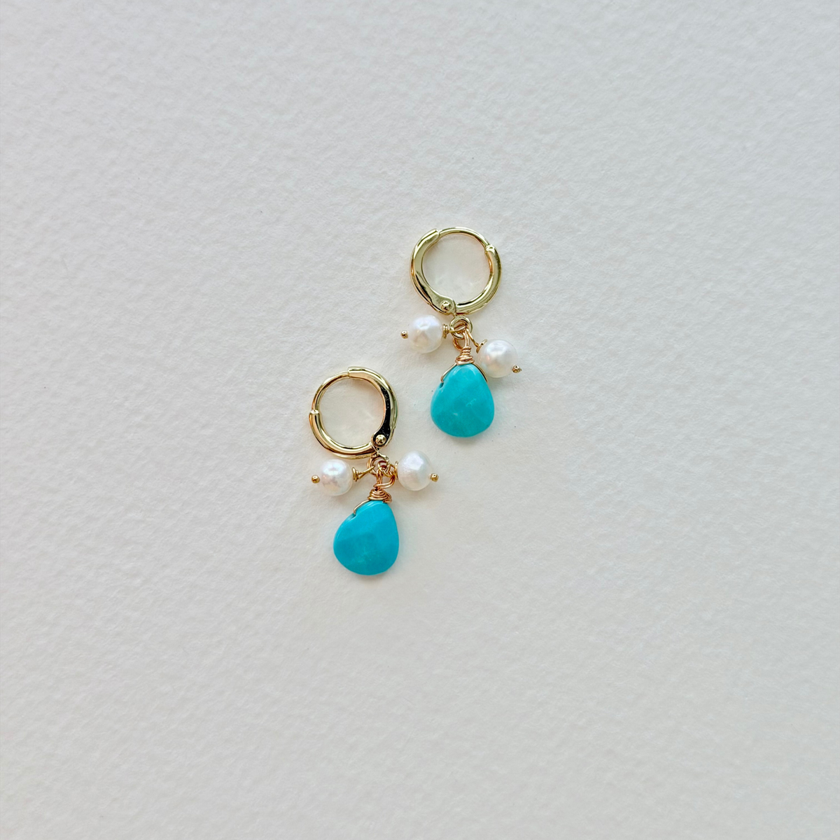 Pair of earrings with turquoise drops and gold hooks on a light gray background