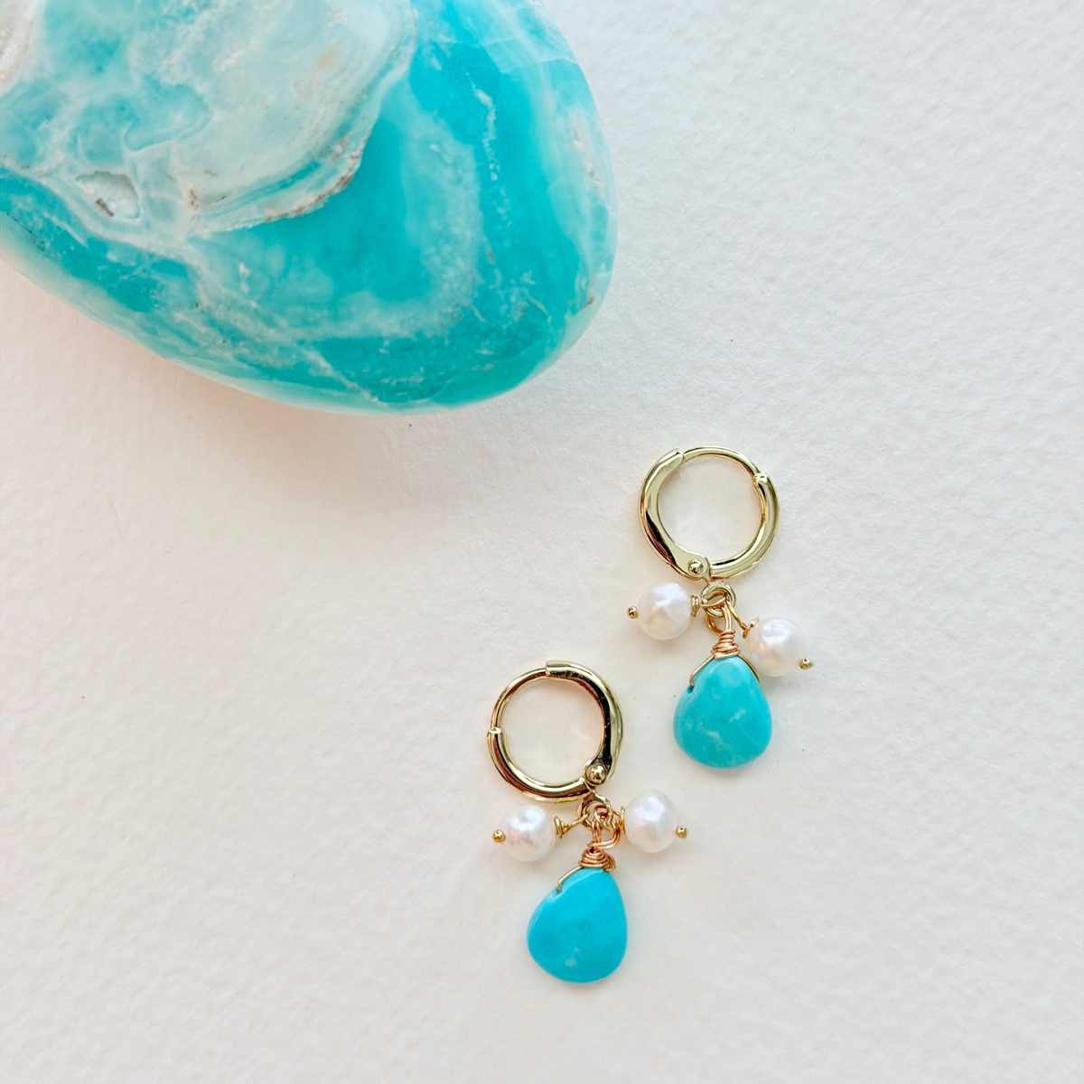 Gold earrings with turquoise stones and pearls on a light background