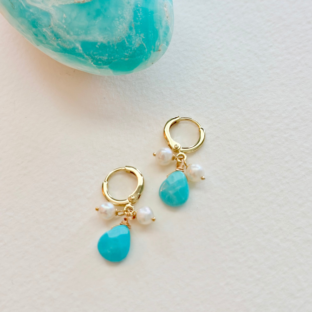 Gold hoop earrings with turquoise teardrop and pearl charms on a light background