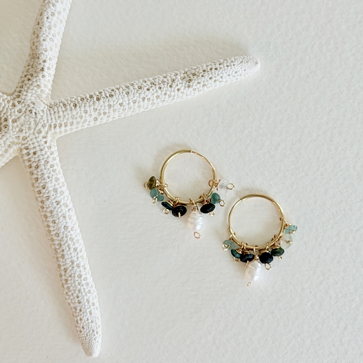 Gold hoop earrings with green and black beads on a white surface with a starfish.