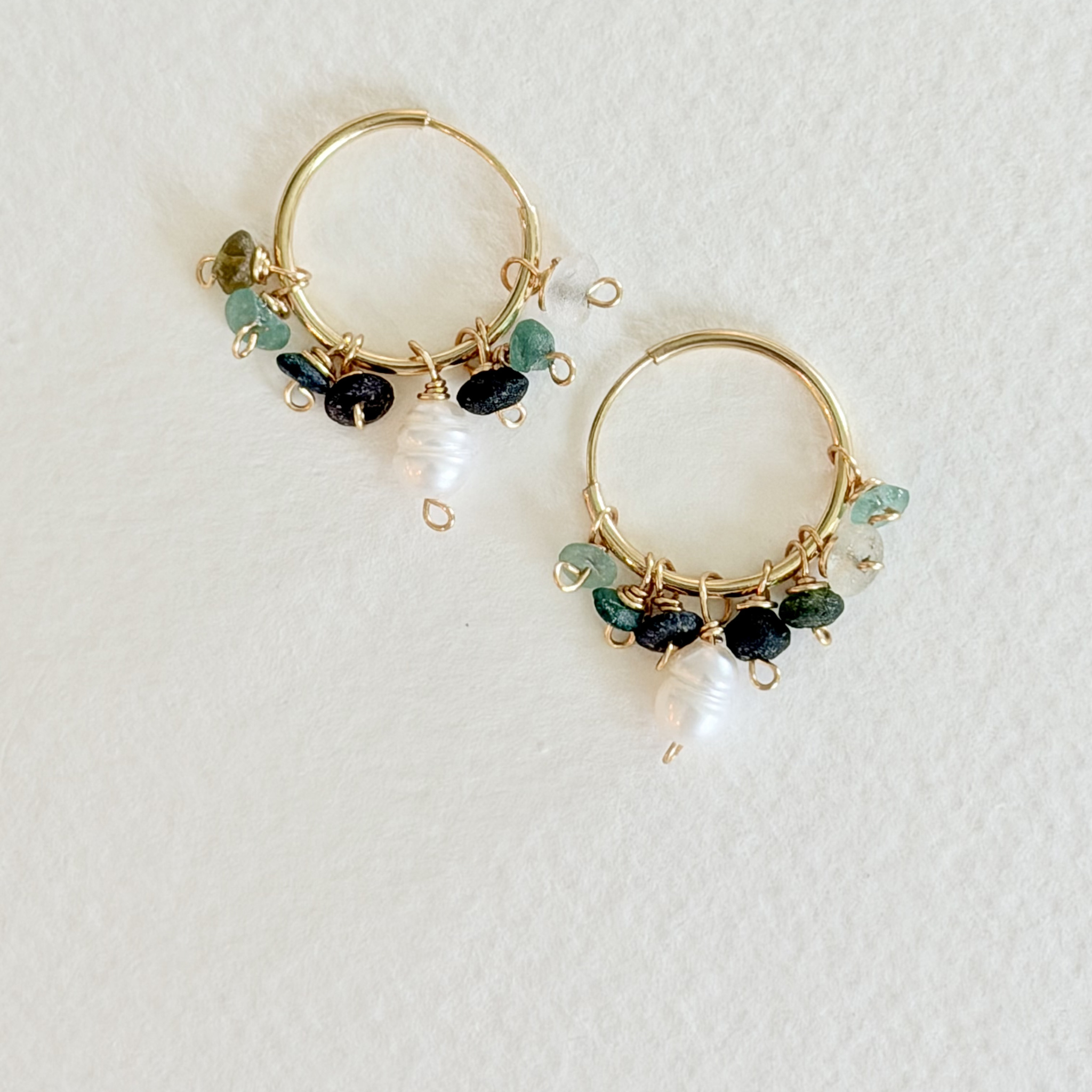 Gold hoop earrings with pearls and green gemstones on a light gray background