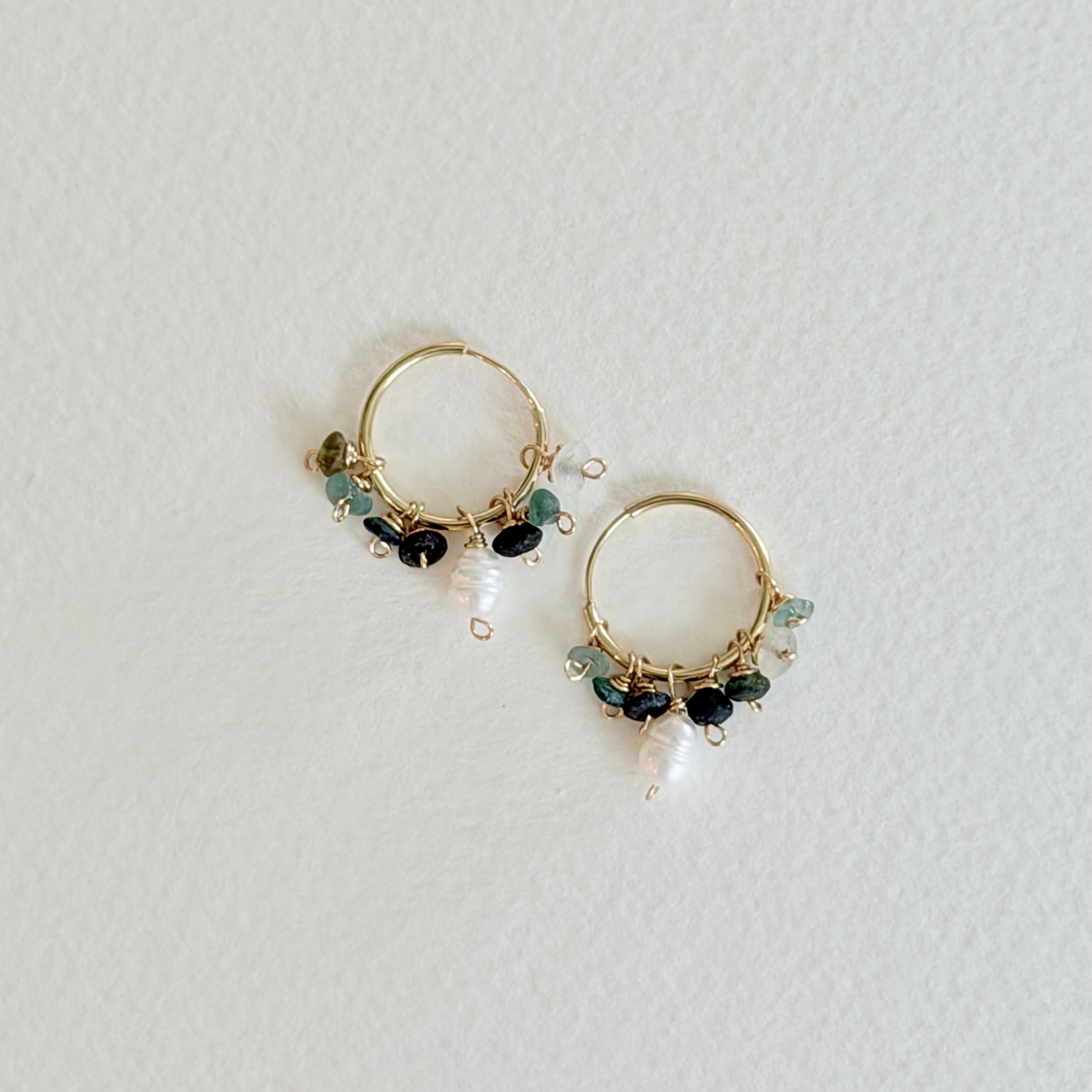 Gold hoop earrings with green and black gemstones on a light gray background