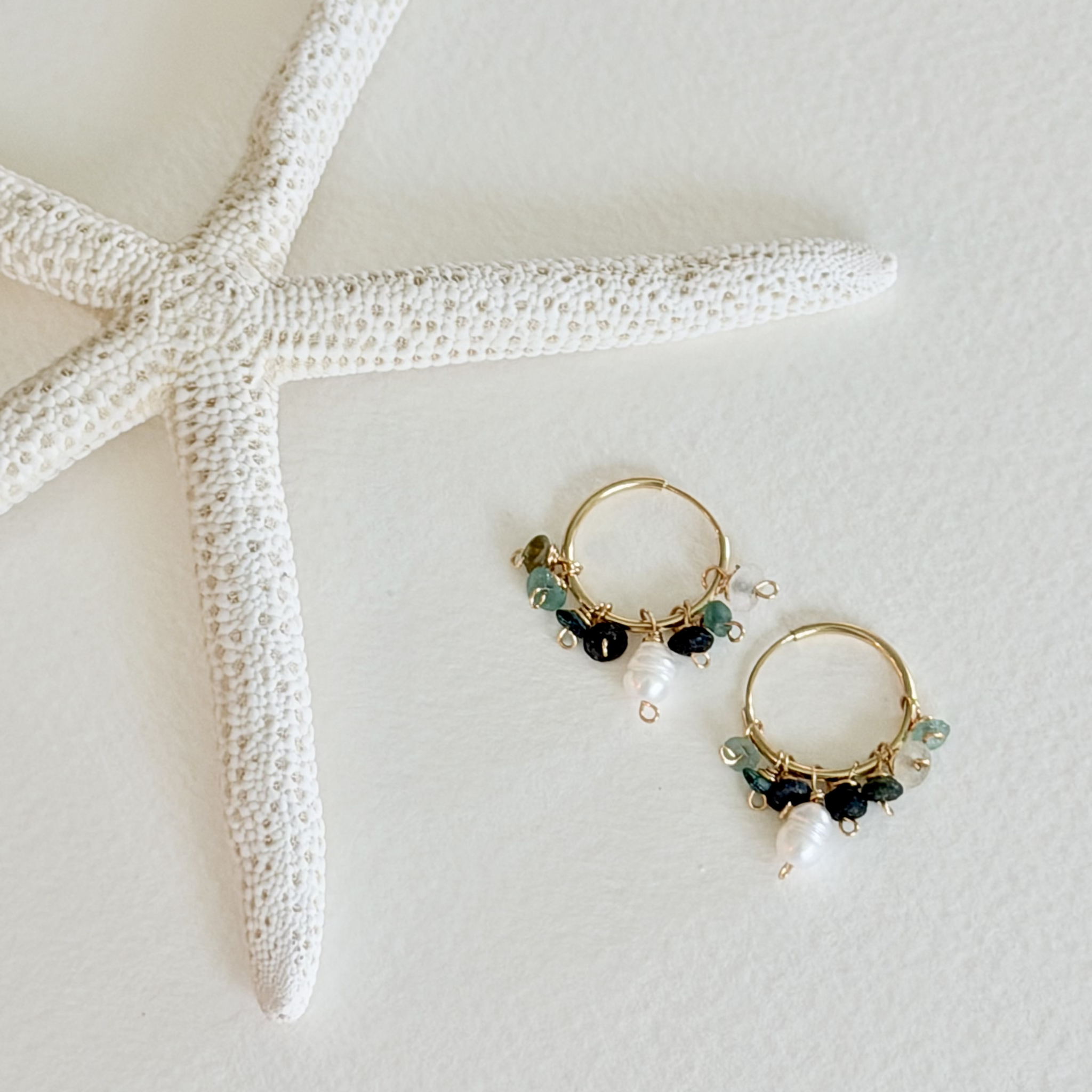 Gold hoop earrings with pearls and gemstones on a white surface with a starfish.