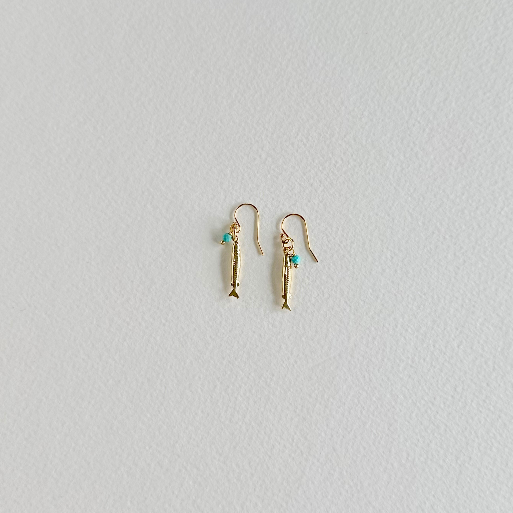 Gold fish-shaped earrings with turquoise stones on a light gray background