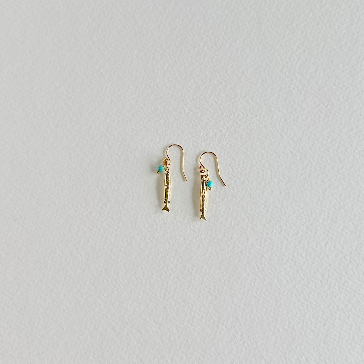 Gold fish-shaped earrings with turquoise stones on a light gray background