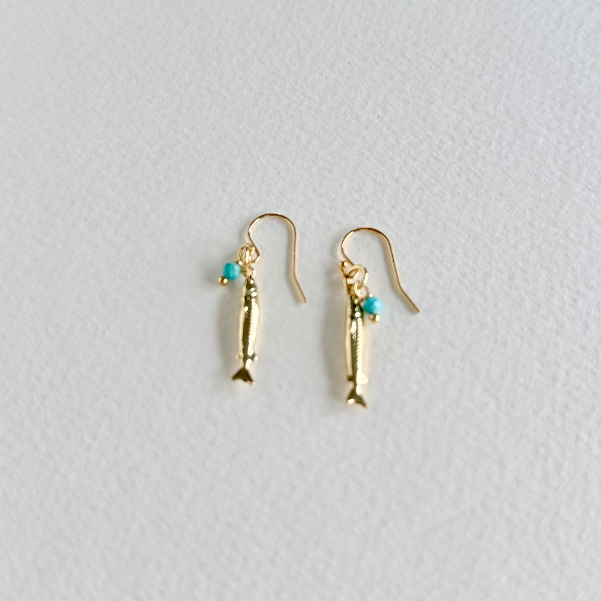Gold fish-shaped earrings with turquoise beads on a light gray background