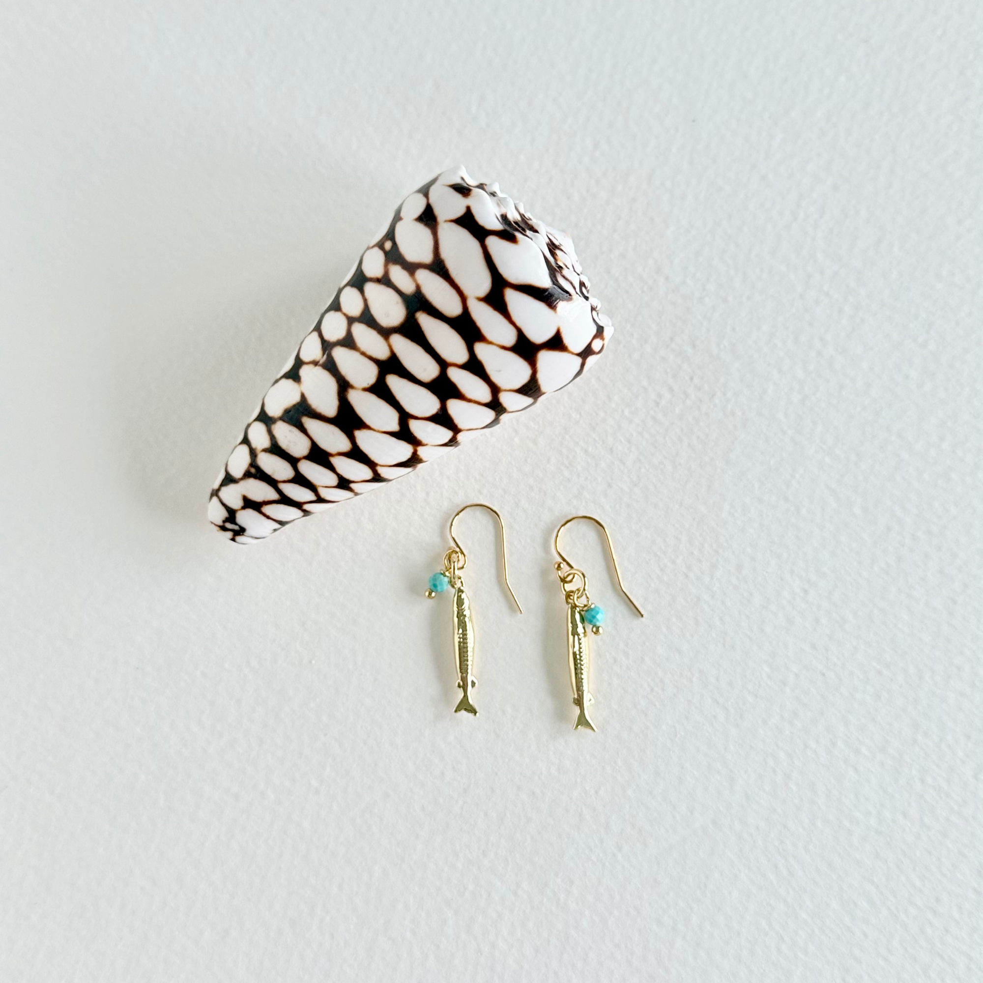 Gold fish earrings with turquoise stones on a white background with a shell.