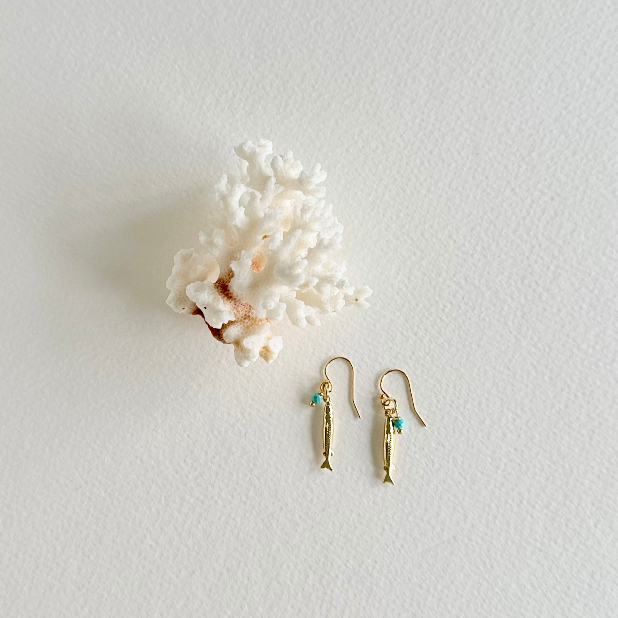 Gold fish-shaped earrings with turquoise stones on a white background with coral.