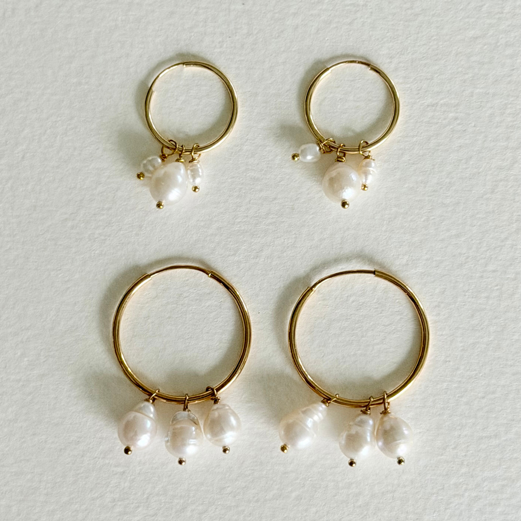 Gold hoop earrings with pearl drops on a light gray background