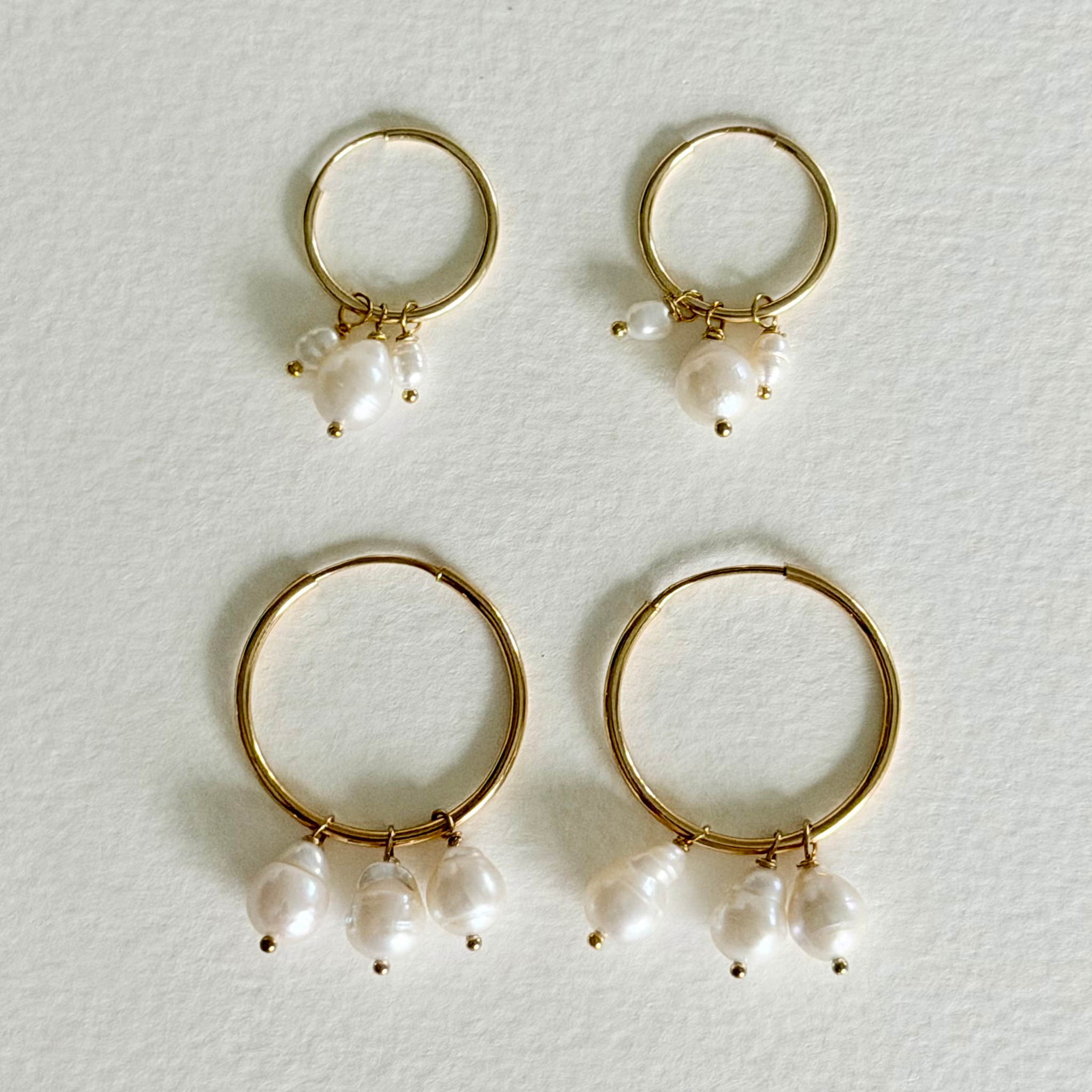 Gold hoop earrings with pearl drops on a light gray background