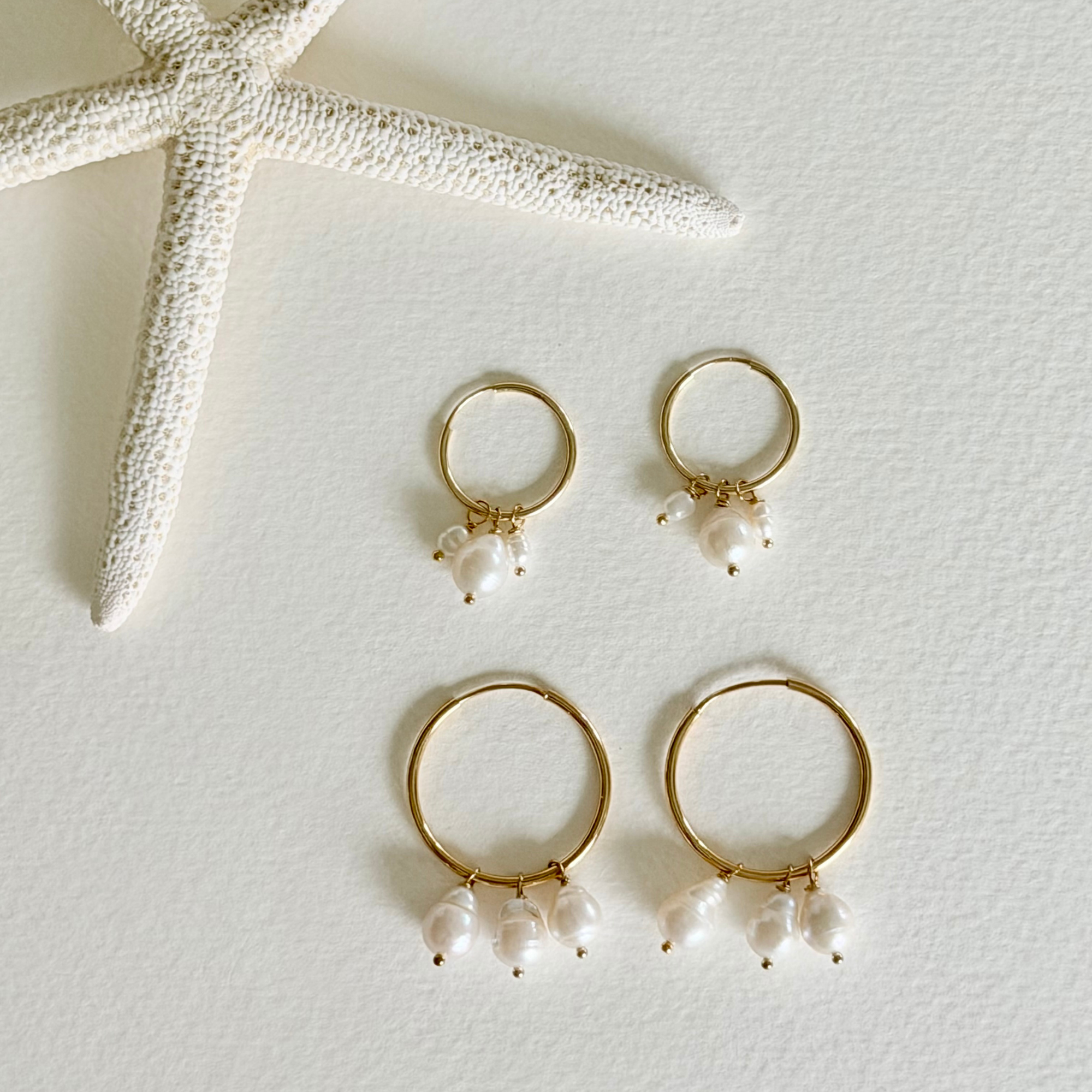 Gold hoop earrings with pearl drops on a light background with a starfish.