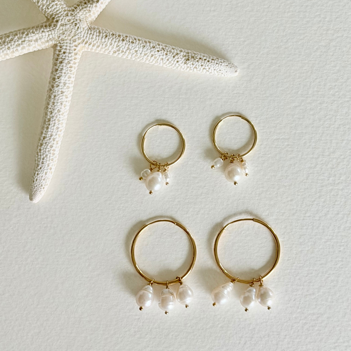Gold hoop earrings with pearl drops on a light background with a starfish.